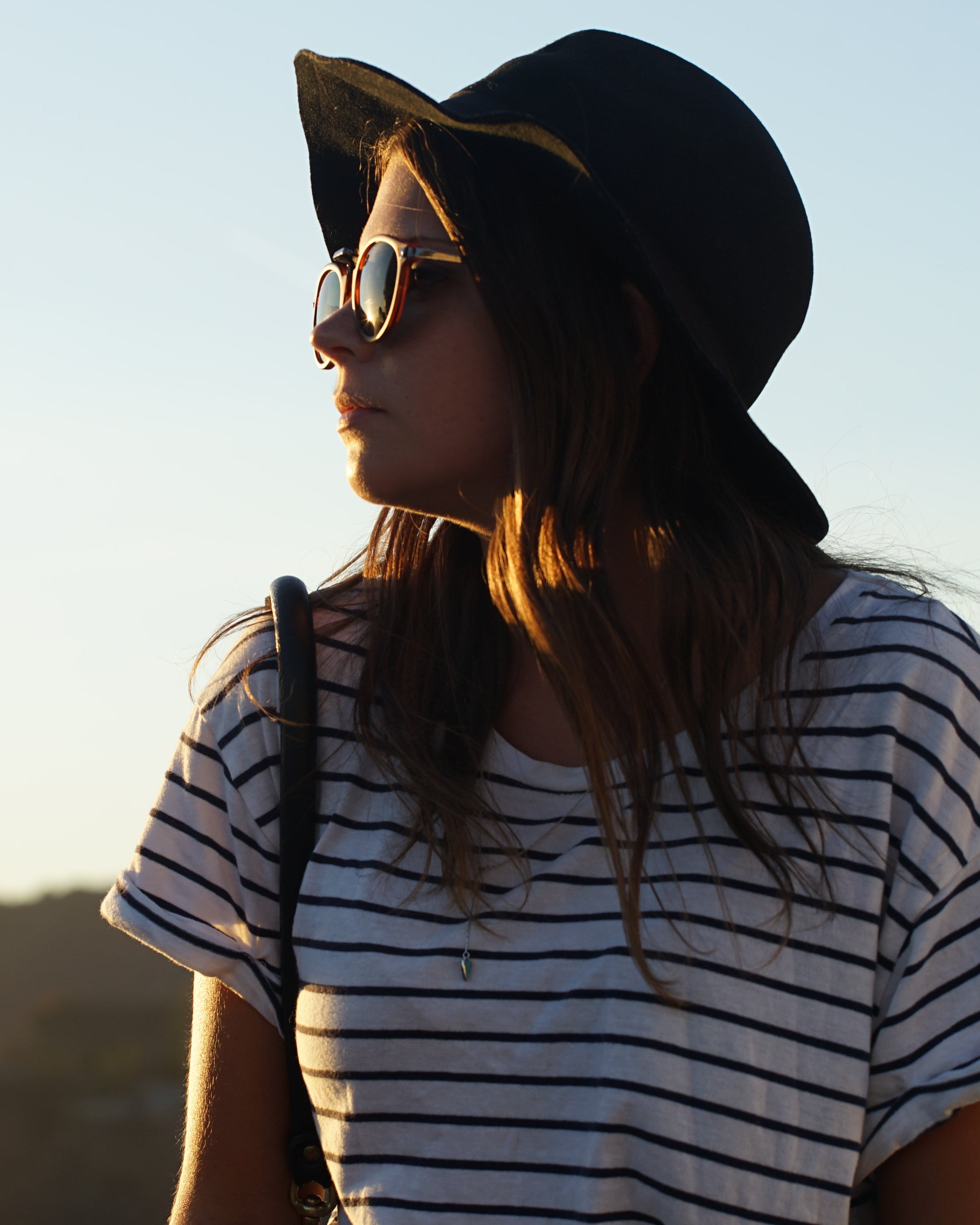 Person wearing a black hat and striped shirt against a mountainous landscape