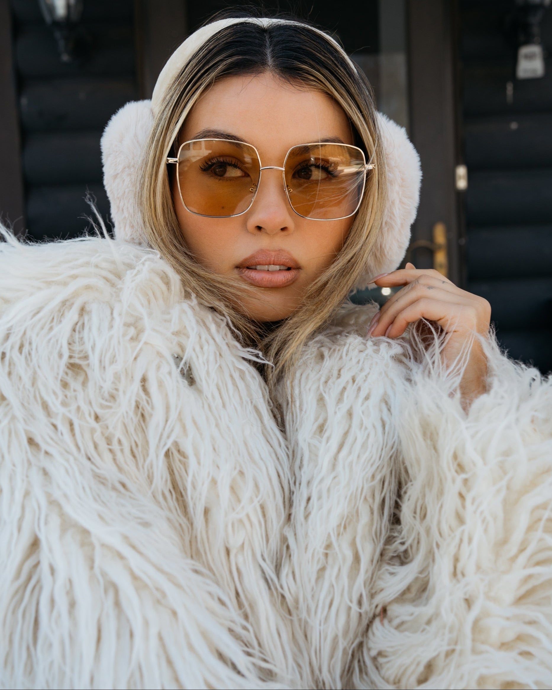 Person wearing a white fluffy coat and sunglasses with a blurred background
