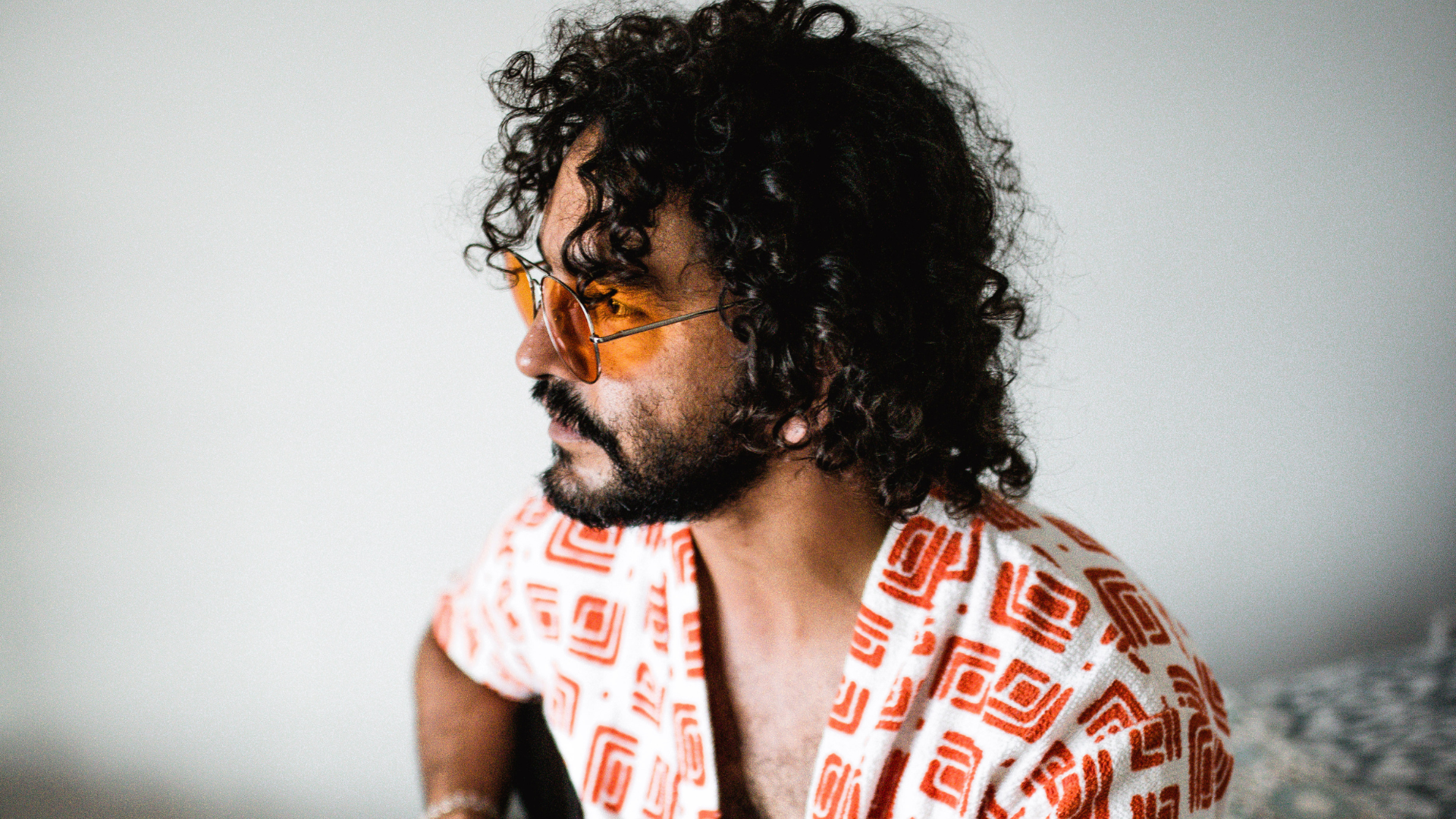 Man with a guitar wearing an orange and white patterned shirt.
