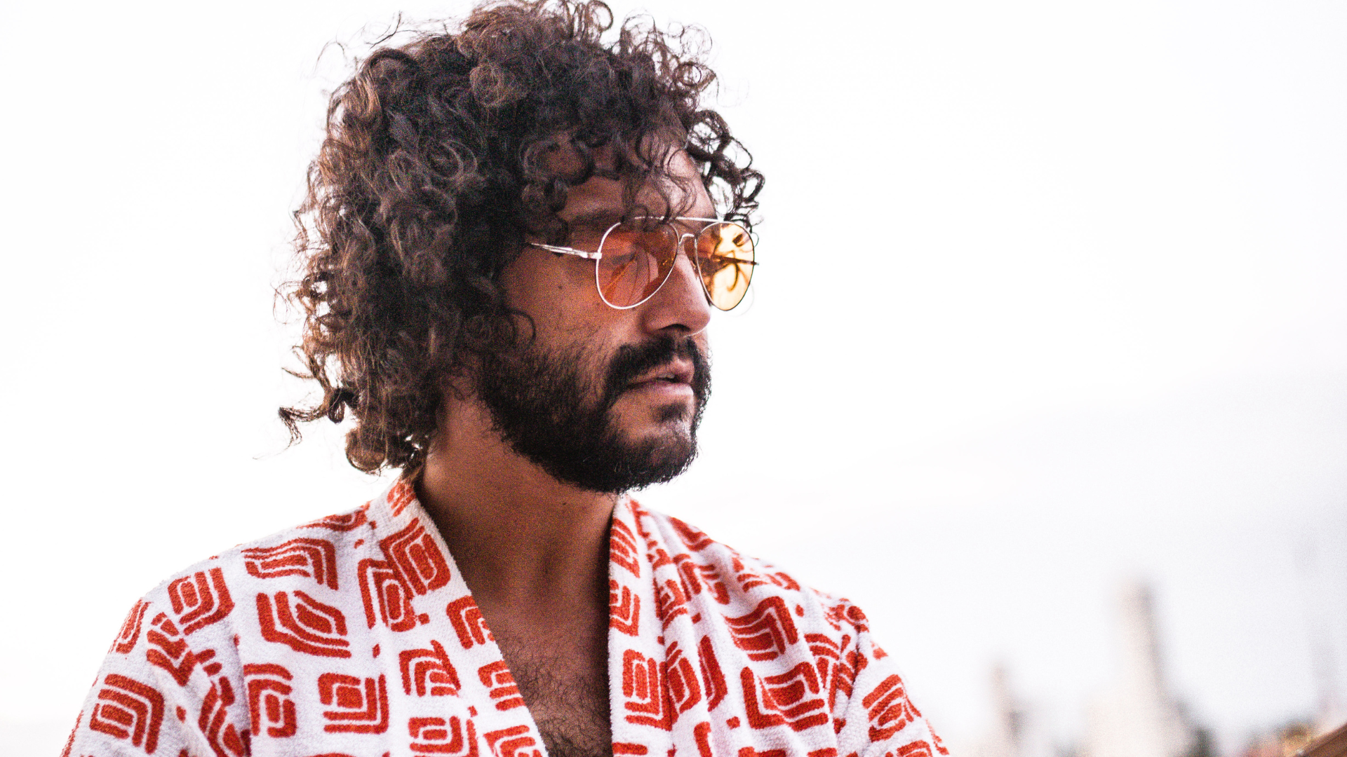 Man with curly hair and a beard wearing a red and white patterned shirt.