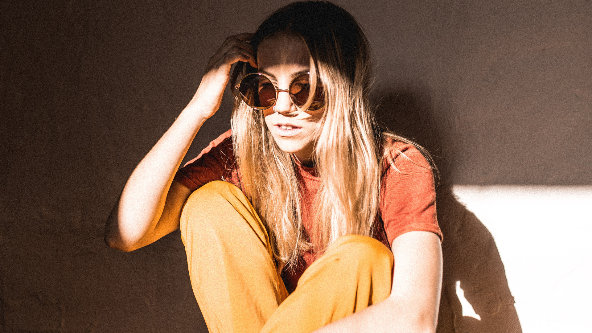 Woman wearing sunglasses and a red top with a yellow skirt against a dark background