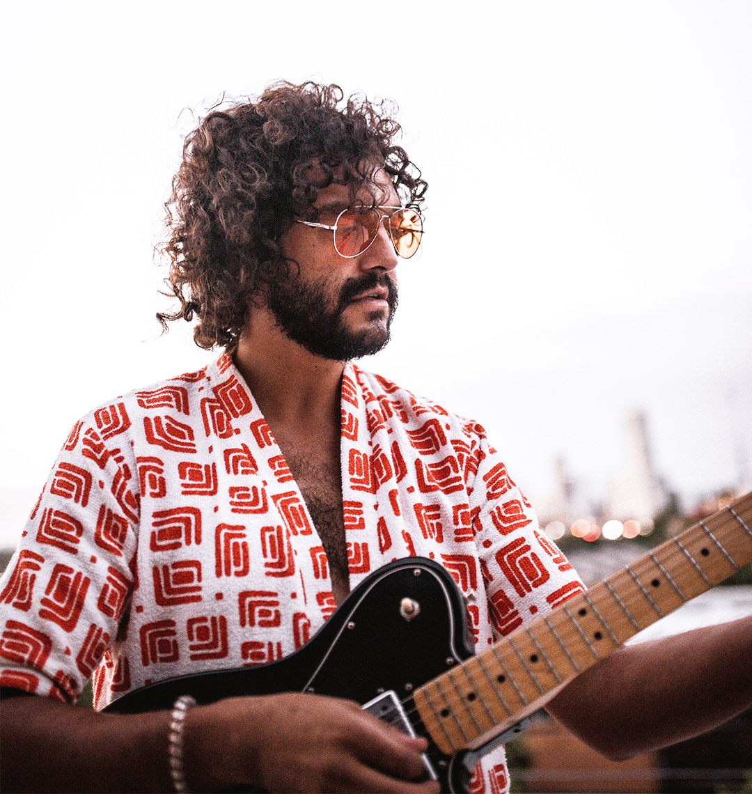 Man playing guitar with a patterned shirt and sunglasses, blurred background